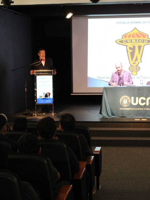 Un evento académico con un orador en el escenario y una audiencia atenta.