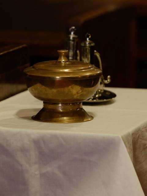 Un recipiente de metal brillante sobre una mesa blanca en un ambiente solemne.