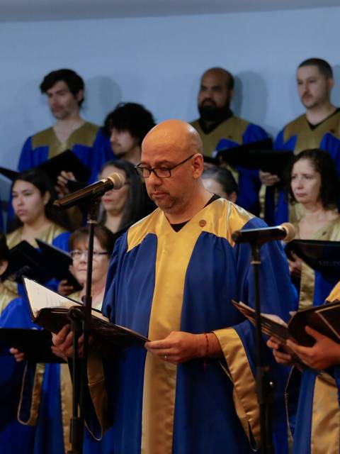 Un coro de personas vestidas con túnicas azules y doradas cantando en un evento.