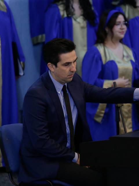 Un pianista acompaña a un coro con trajes azules en una presentación.