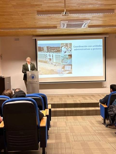 Un caballero presenta una charla frente a un grupo de personas en una sala de conferencias.