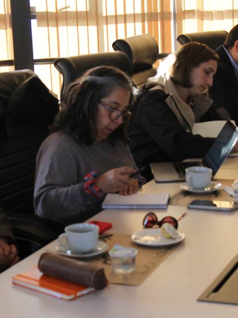 Una reunión de trabajo con varias personas tomando apuntes y un café.