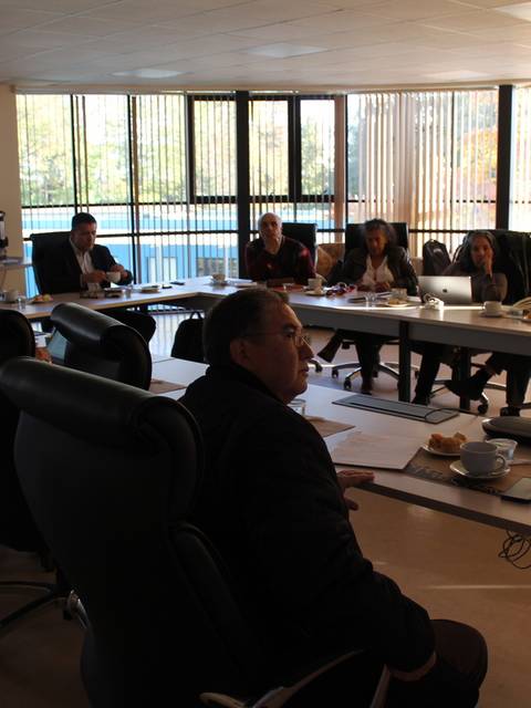 Una reunión de trabajo en una sala con varias personas sentadas alrededor de una mesa.