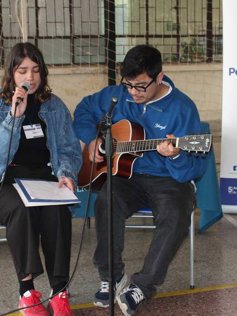 Un par de estudiantes se presentan en un evento cultural, uno cantando y el otro tocando la guitarra.