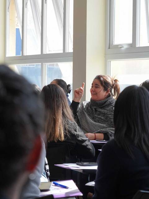 Una mujer está hablando frente a un grupo en una sala iluminada.