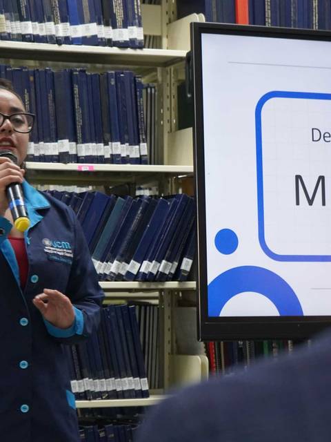 Una joven expone frente a un público en una biblioteca.