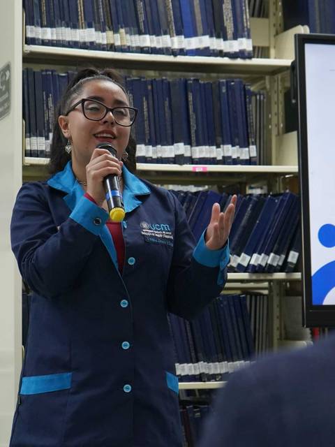 Una persona está presentando en una biblioteca mientras sostiene un micrófono.