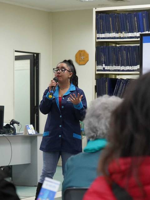 Una mujer presenta sobre microcuentos frente a un grupo de personas en una sala.