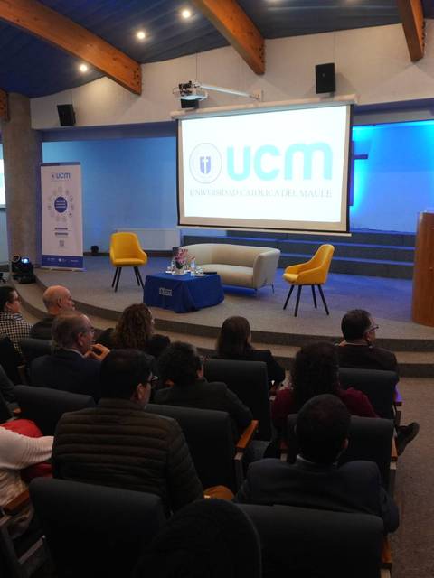 Un evento académico en la UCM con un público atento y un expositor en el escenario.