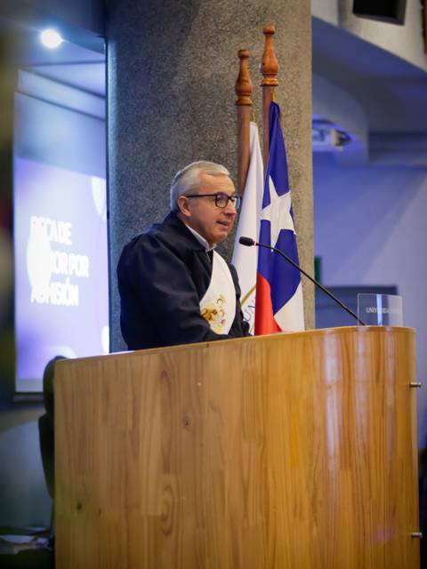 Un orador se presenta en un escenario con banderas chilenas de fondo.