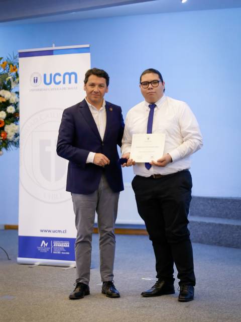 Dos personas posando en un evento de premiación en una sala con fondo decorado.