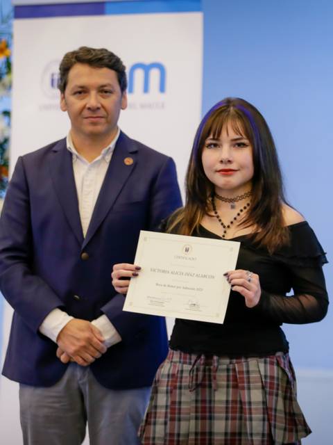 Una chica sonriente sostiene un certificado junto a un hombre en un evento formal.