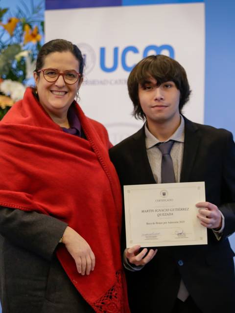 Un joven recibe un reconocimiento en una ceremonia con un ramo de flores de fondo.
