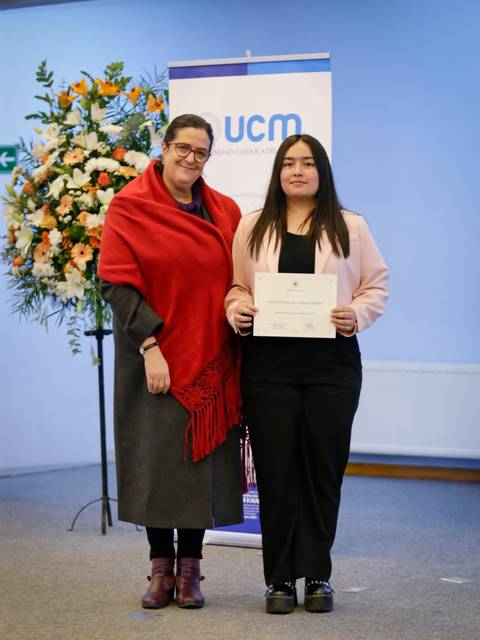 Una ceremonia de entrega de certificado, donde dos mujeres posan sonrientes en un ambiente festivo.