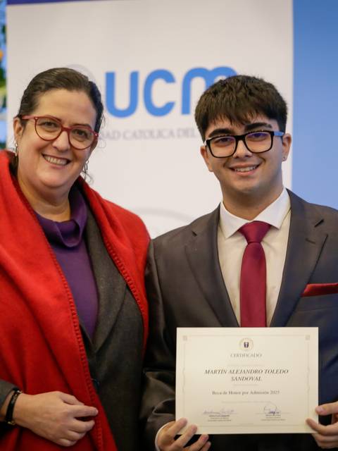 Un joven recibe un reconocimiento en una ceremonia oficial con una mujer a su lado.
