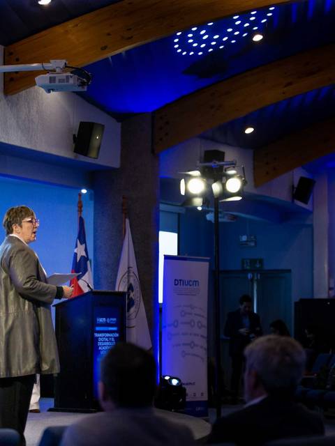 Una presentación en un auditorio donde una persona habla frente a un público atento.
