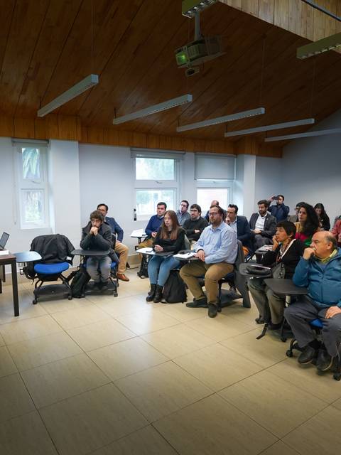 Una presentación en una sala llena de gente escuchando atentamente al expositor.