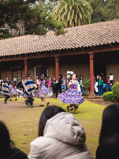 Un grupo de bailarines en trajes tradicionales se presenta en un evento cultural en un patio rodeado de espectadores.