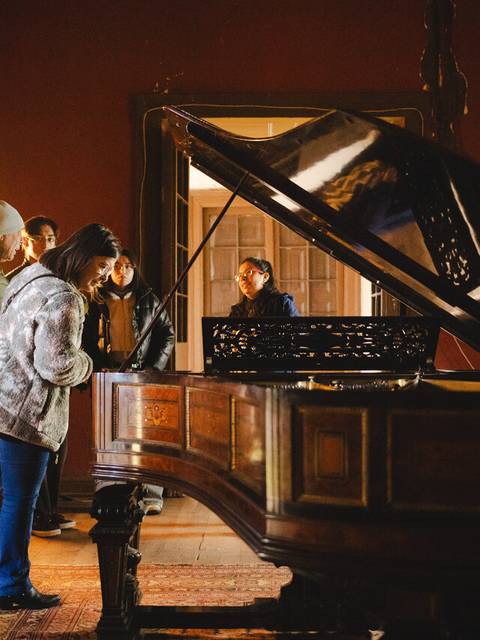 Un grupo de personas se reúne alrededor de un piano antiguo en una habitación iluminada.