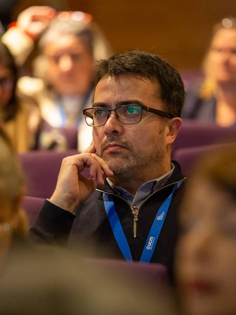 Un hombre pensativo en una conferencia rodeado de otros asistentes.