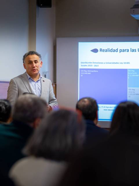 En la imagen, un presentador expone sobre la realidad de las universidades en regiones ante un público atento.