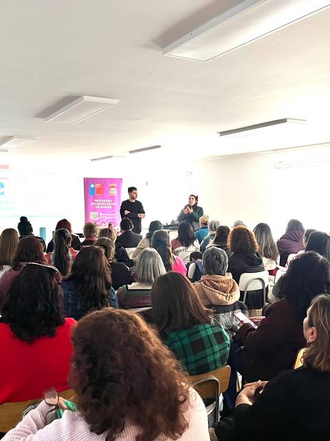 Un grupo grande de personas asiste a una charla en un salón luminoso.