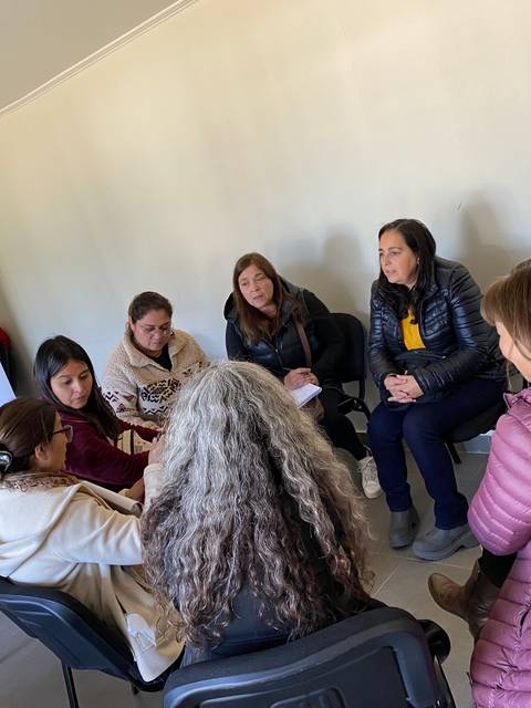 Un grupo de personas conversando en una sala, con un cartel de una universidad al fondo.