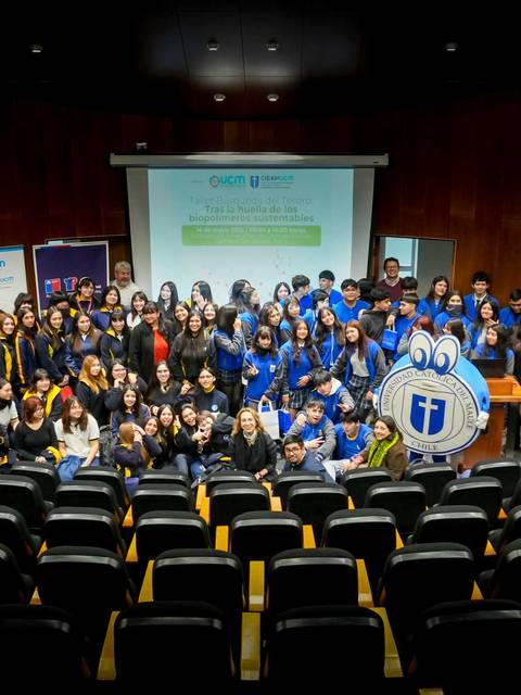 Un grupo grande de estudiantes y profesores celebrando un evento académico en una sala de conferencias.
