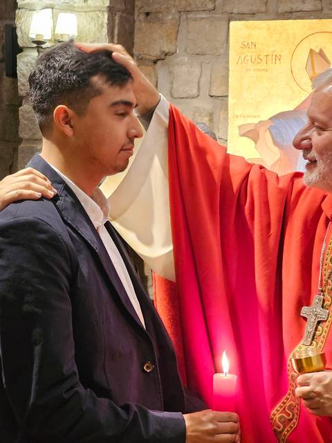 Un joven está siendo bendecido en una ceremonia religiosa por un obispo, mientras otro hombre lo apoya.