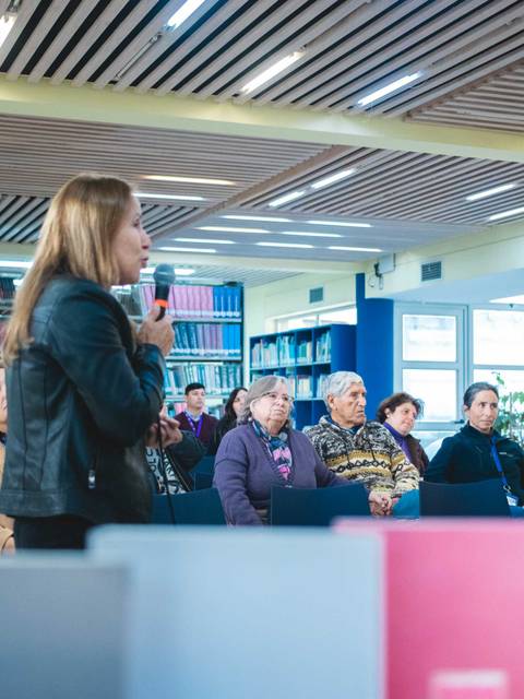Una mujer está hablando frente a una audiencia en una biblioteca.