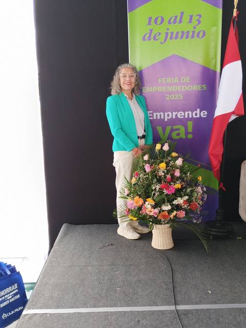 Una mujer sonriente posa junto a un ramo de flores en un evento de emprendimiento.