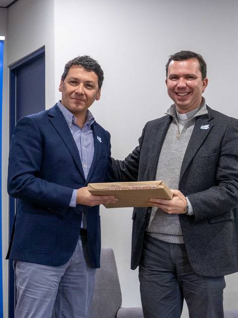 Dos hombres se están saludando y entregando un objeto en un evento oficial.