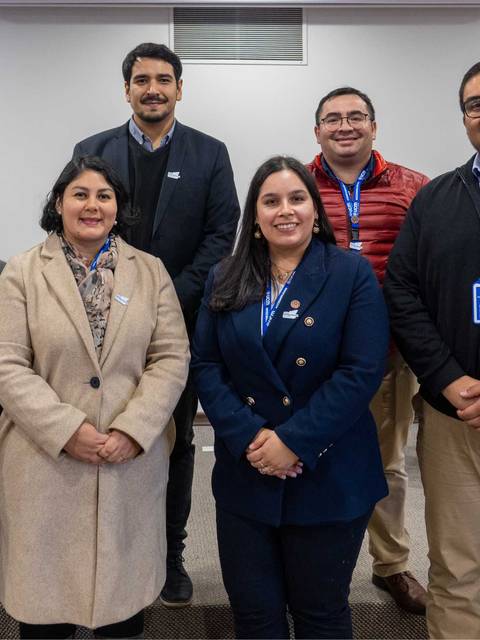 Un grupo de seis personas posando en una sala con banderas de Chile de fondo.