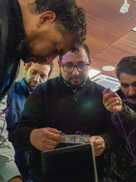 Un grupo de hombres se encuentra enfocado en un proyecto técnico, colaborando en la manipulación de componentes electrónicos.