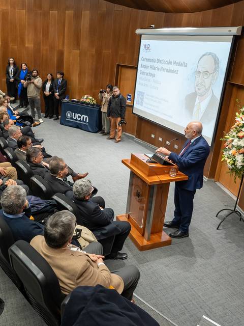 Un evento académico con un orador principal frente a un público atento en un auditorio chileno.