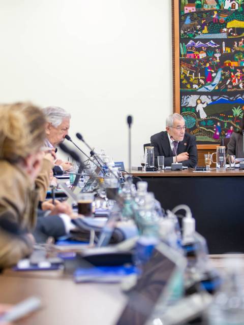 Una reunión formal con varias personas conversando y un mural colorido al fondo.