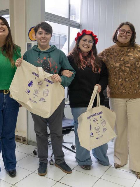 Un grupo de cuatro jóvenes sonrientes posando con bolsas de tela en un espacio interior.