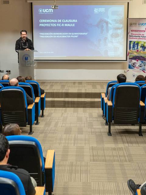 Un hombre está hablando en un evento mientras una audiencia lo escucha atentamente.