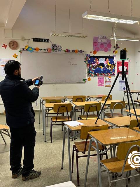 Un cabro está grabando en un curso con escritorios y decoraciones en la pared.