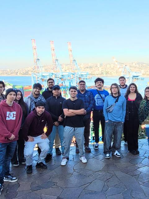 Un grupo de personas posando en un mirador con vista al puerto y sus grúas en Valparaíso.