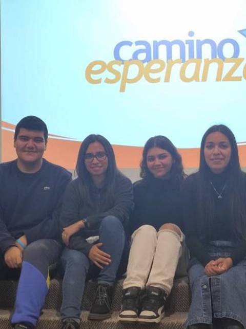 Un grupo de jóvenes sonrientes posando frente a una presentación del programa 'Camino a la Esperanza'.