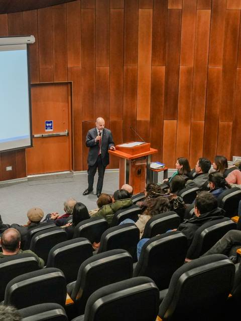Una charla en un auditorio con un ponente frente a una audiencia atenta.
