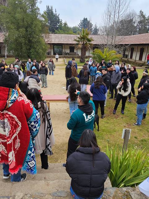 Un grupo de personas se reúne en un espacio abierto, con un ambiente natural y edificios alrededor.