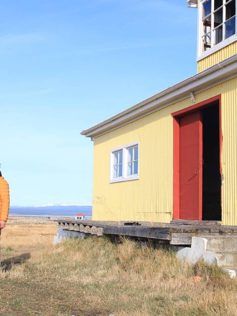 Dos hombres conversando frente a una casa amarilla en un paisaje patagónico.