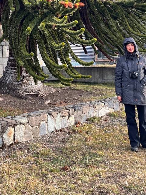 Una mujer posa sonriente al lado de un árbol en un paisaje chileno.