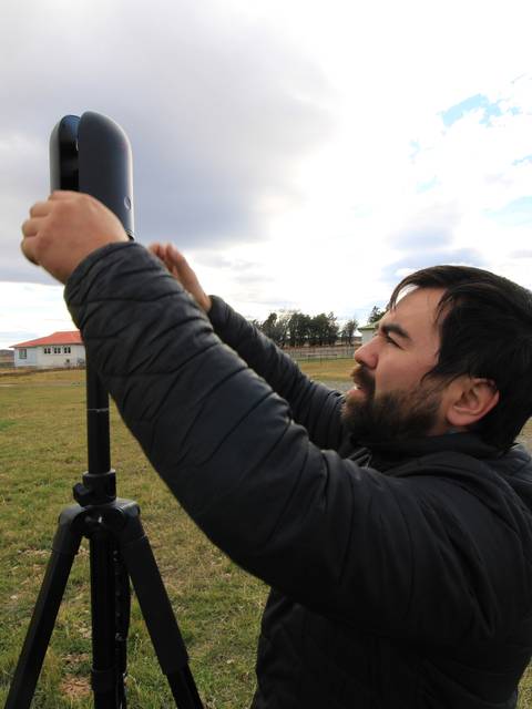 Un hombre está ajustando un equipo en un trípode en un paisaje chileno.