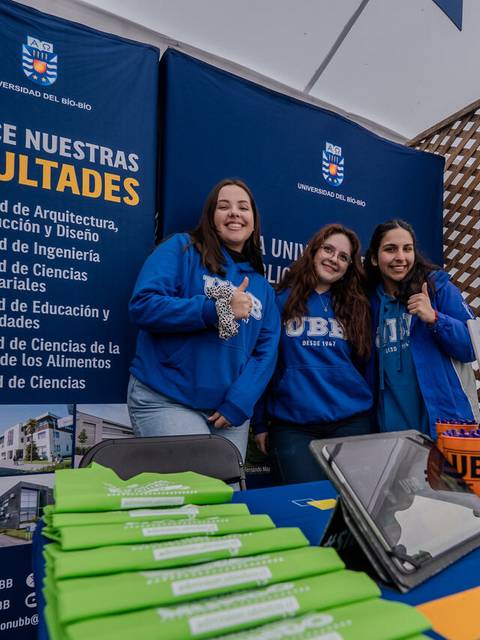 Tres estudiantes sonrientes representan a la Universidad del Bío-Bío en una feria de facultades.