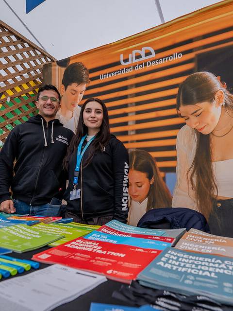 Un par de estudiantes sonríen en un stand de la Universidad del Desarrollo durante una feria educativa.