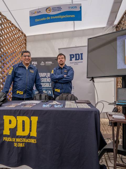 Dos funcionarios de la PDI posan en un stand informativo en una actividad pública.