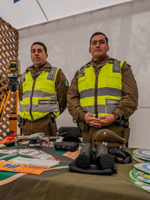 Dos carabineros posan en un stand con equipo policial y material informativo.
